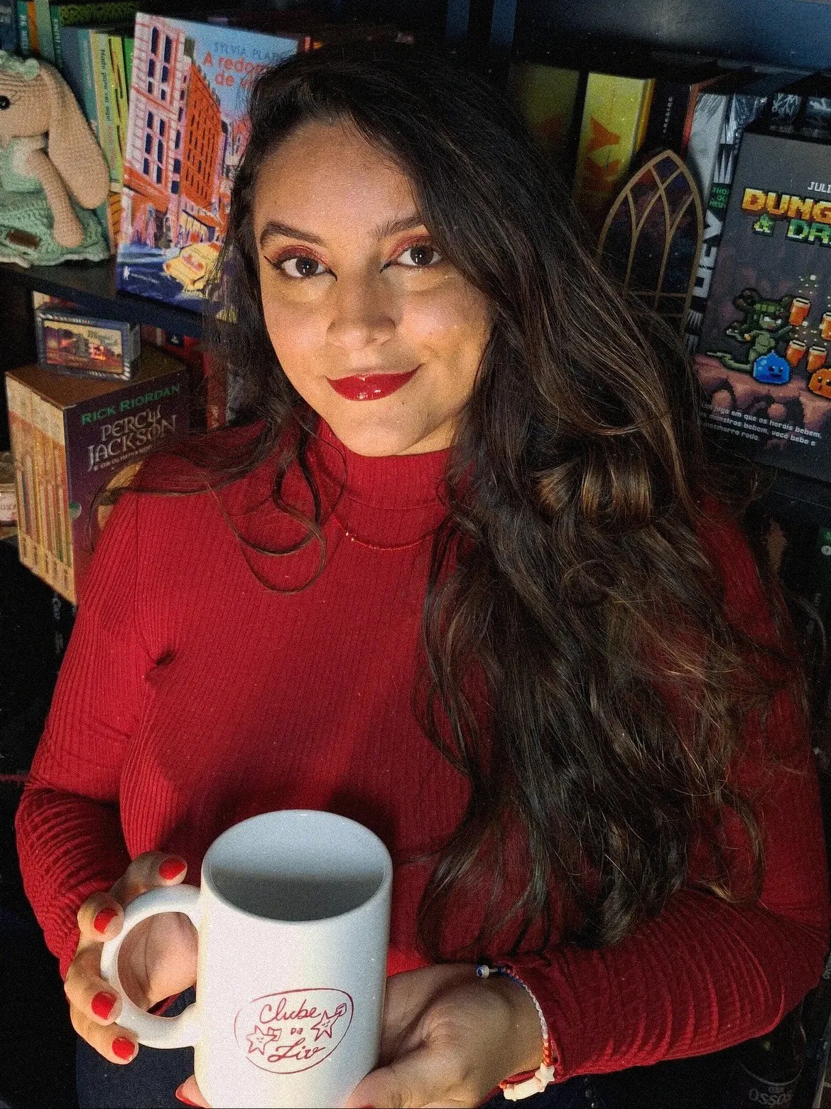 Mayara Trevizani com uma caneca do clube do livro diante de sua estante